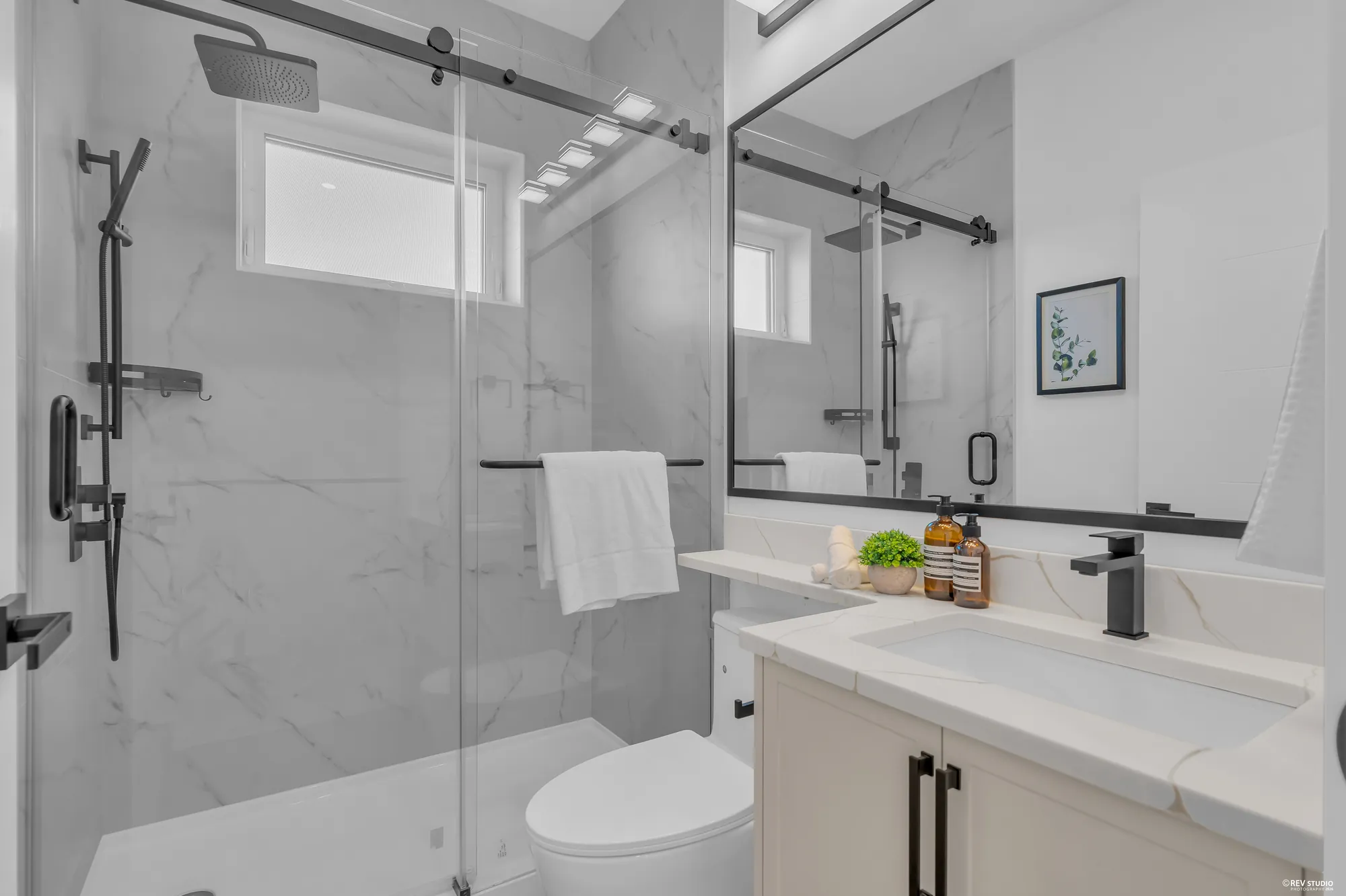 The hall bathroom: a glass shower in marble-look tile, a window, a white vanity with a black tap