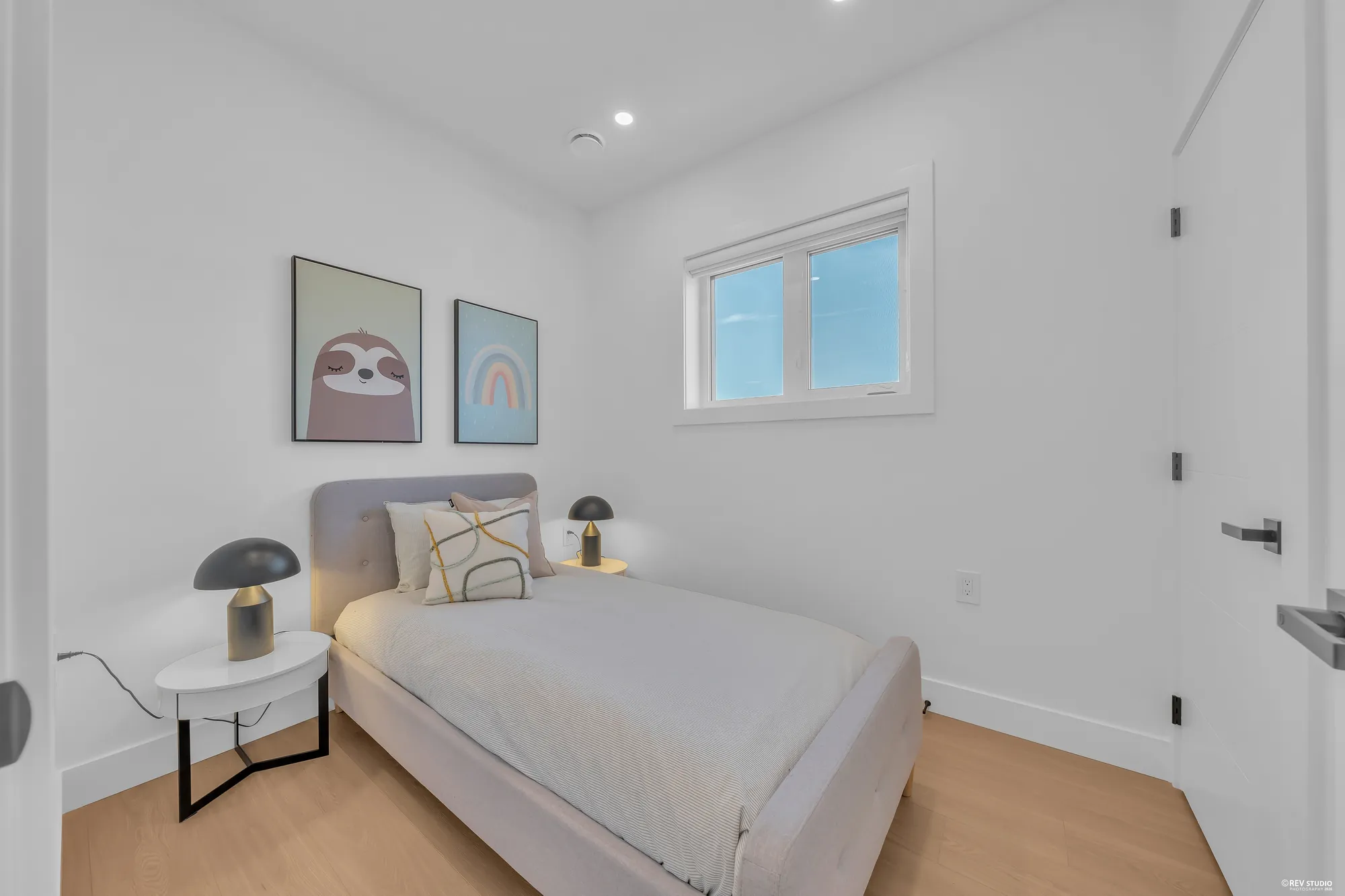 The third bedroom: a single bed with a lamp on a small table, two prints, a high window