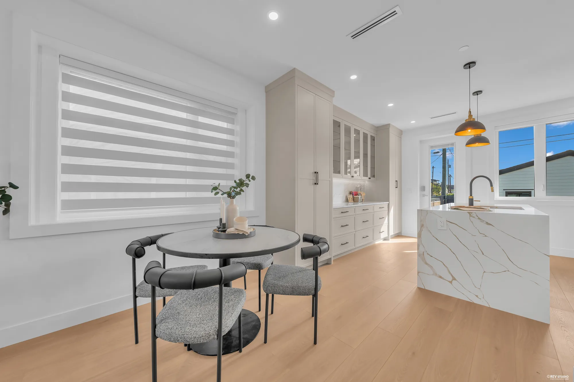 The dining table beside the kitchen island, a window with its blinds behind