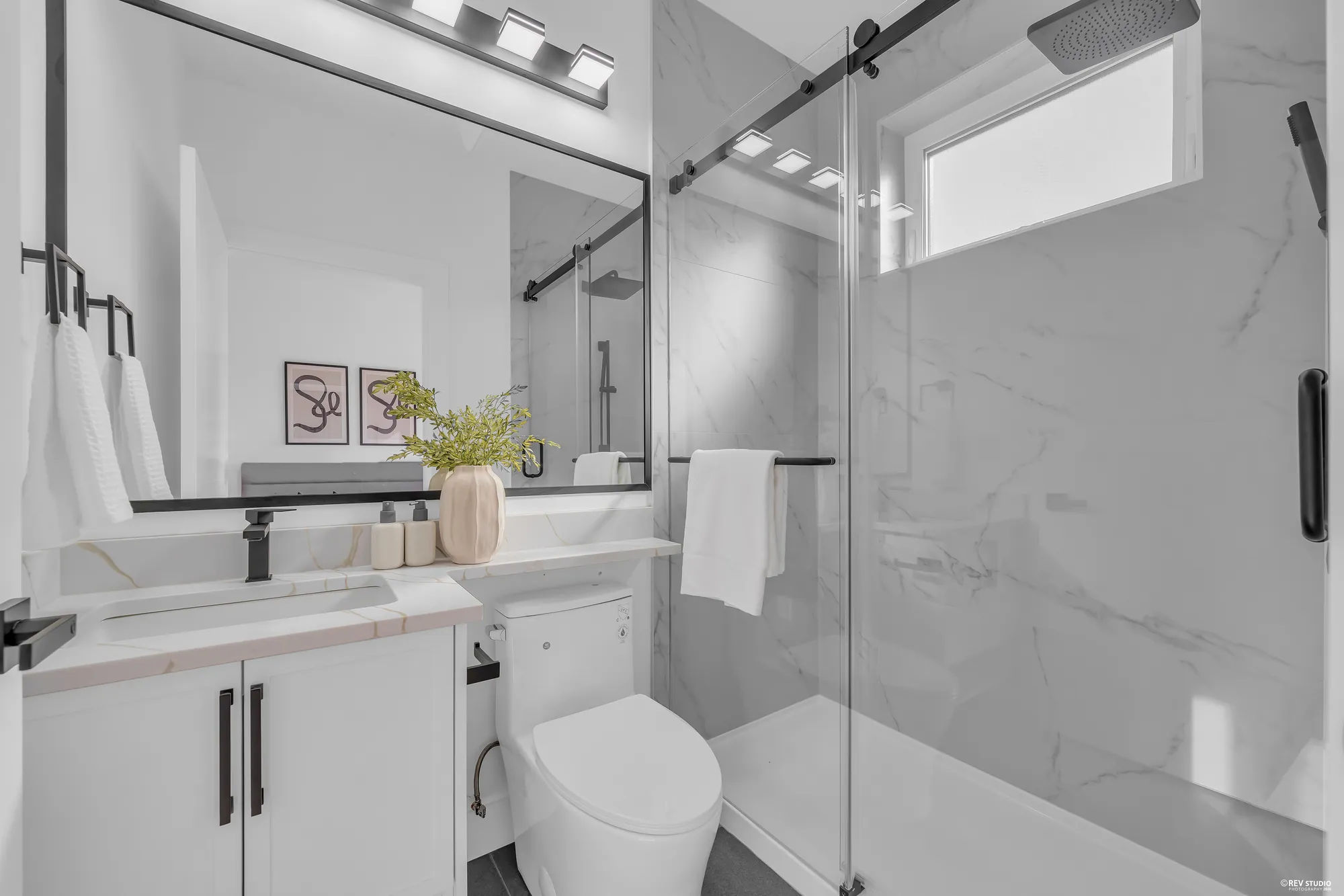 The primary bathroom: a glass shower in marble-look tile, a white vanity, a window