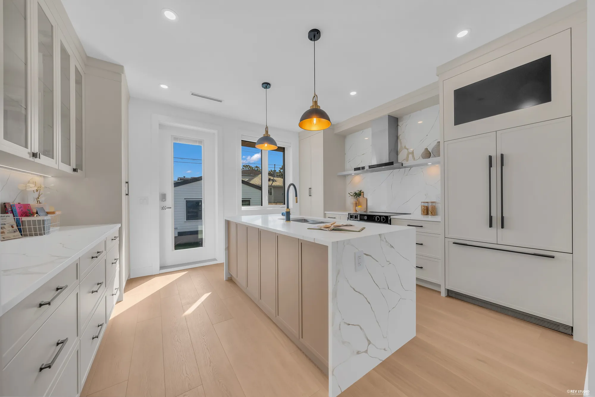 The kitchen: taupe cabinets, a marble-look quartz island with a waterfall end, brass pendants, a panelled fridge, the range under its hood, the door to the back porch