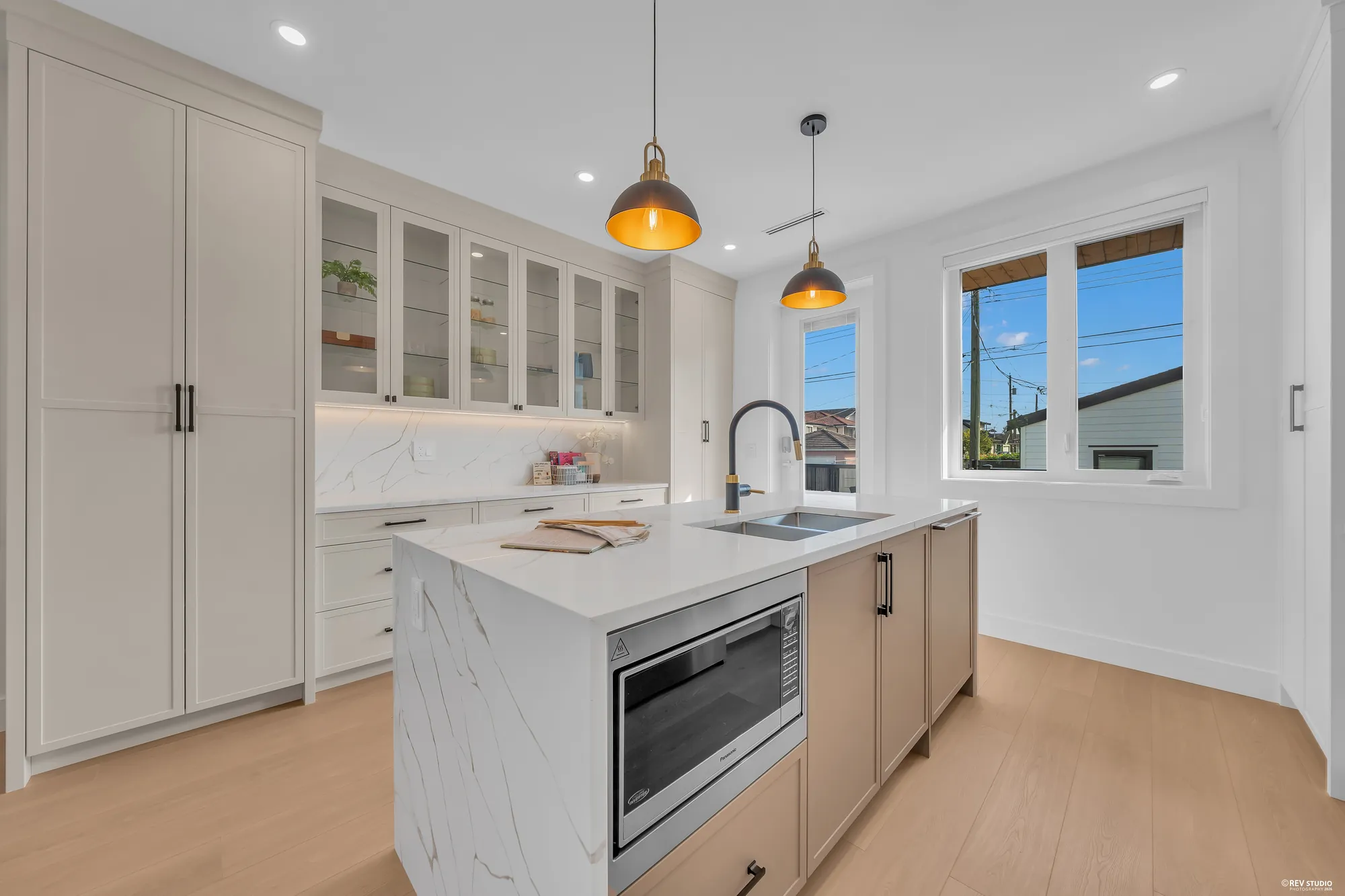 The island end with the microwave drawer, glass-fronted upper cabinets, the window