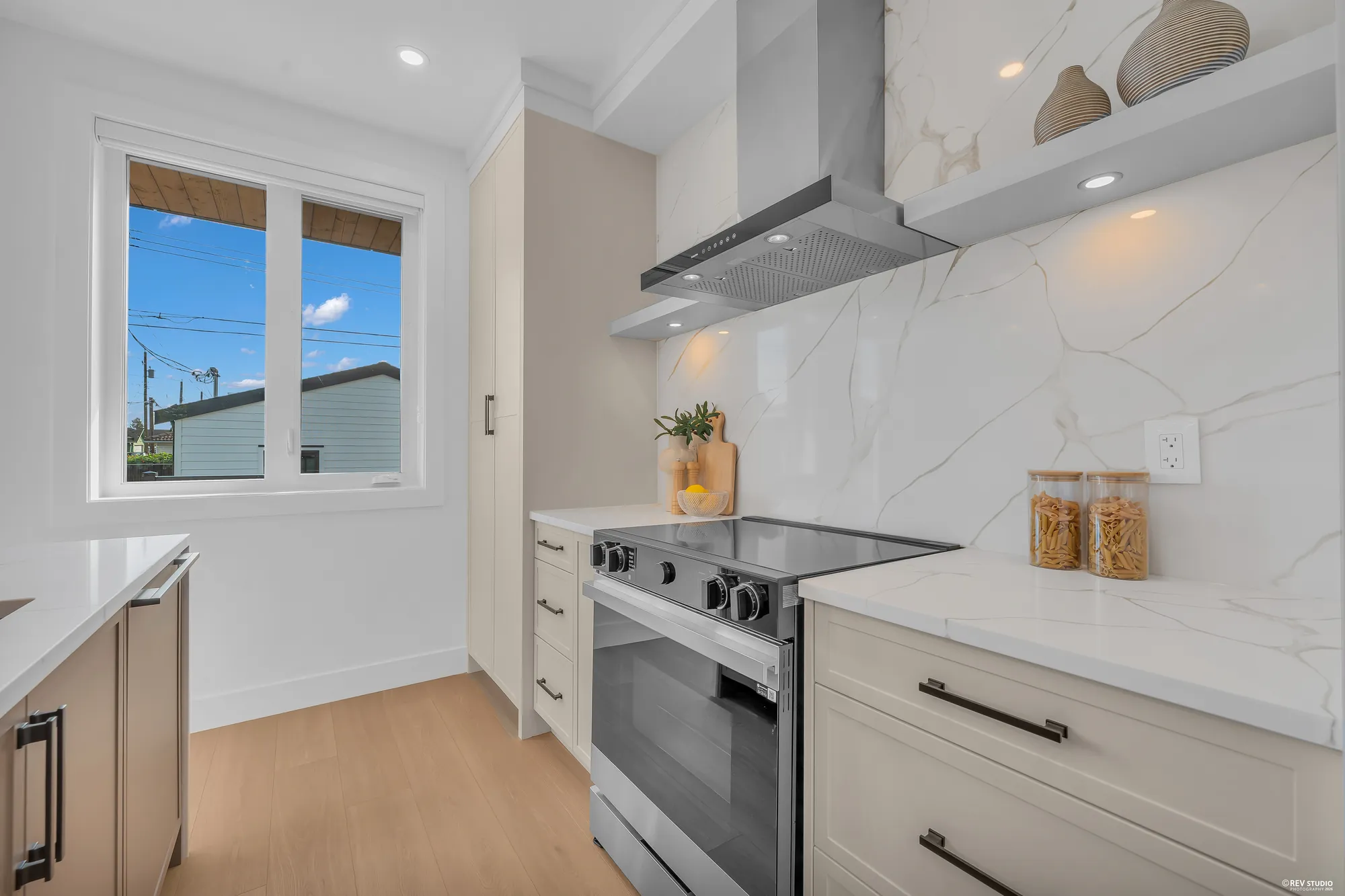 The range under its hood, the window beside it, the tall pantry cabinets