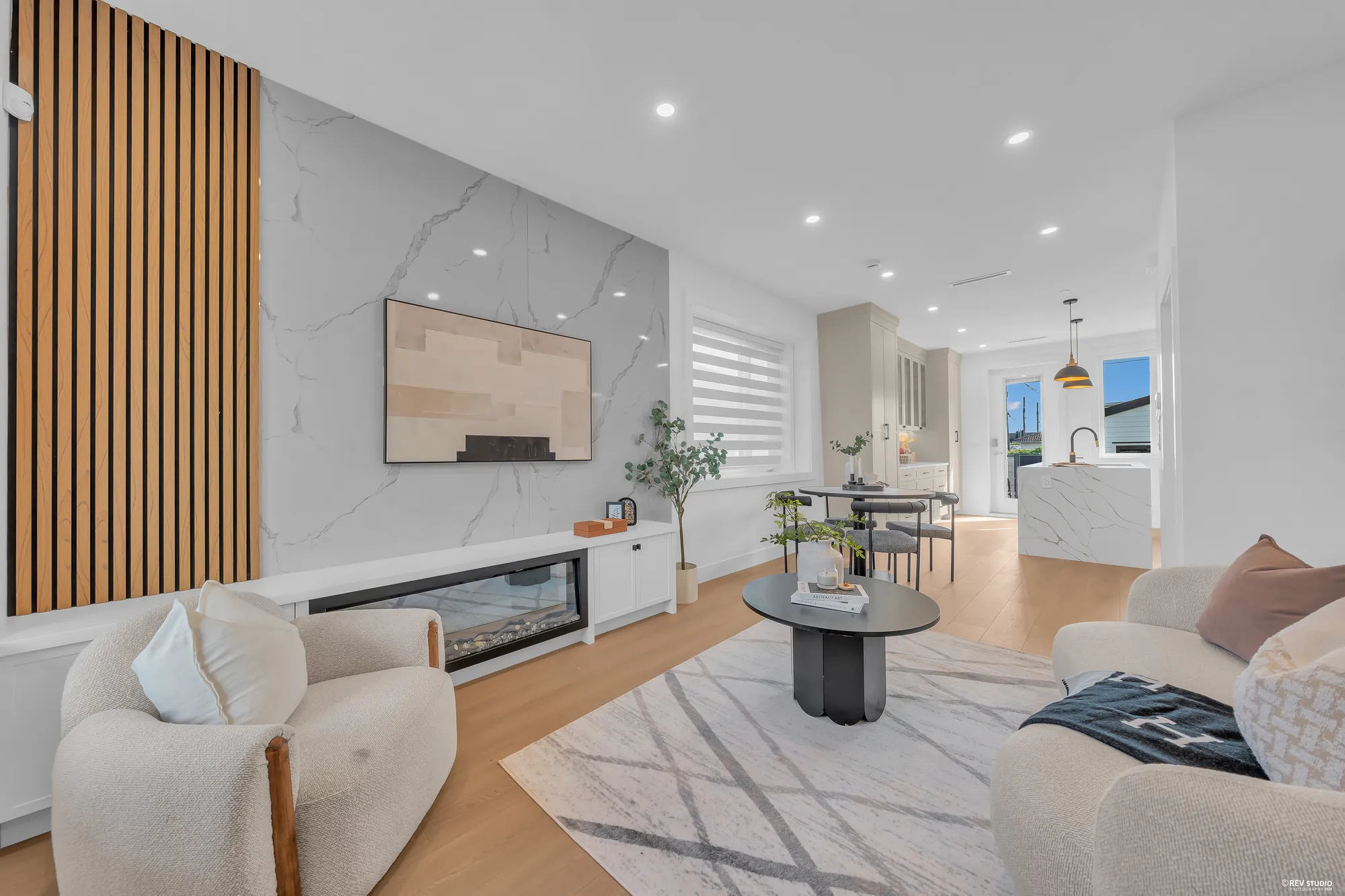 The living room: an electric fireplace in a marble surround under a wall of wood slats, a curved armchair on a rug, the window to the street