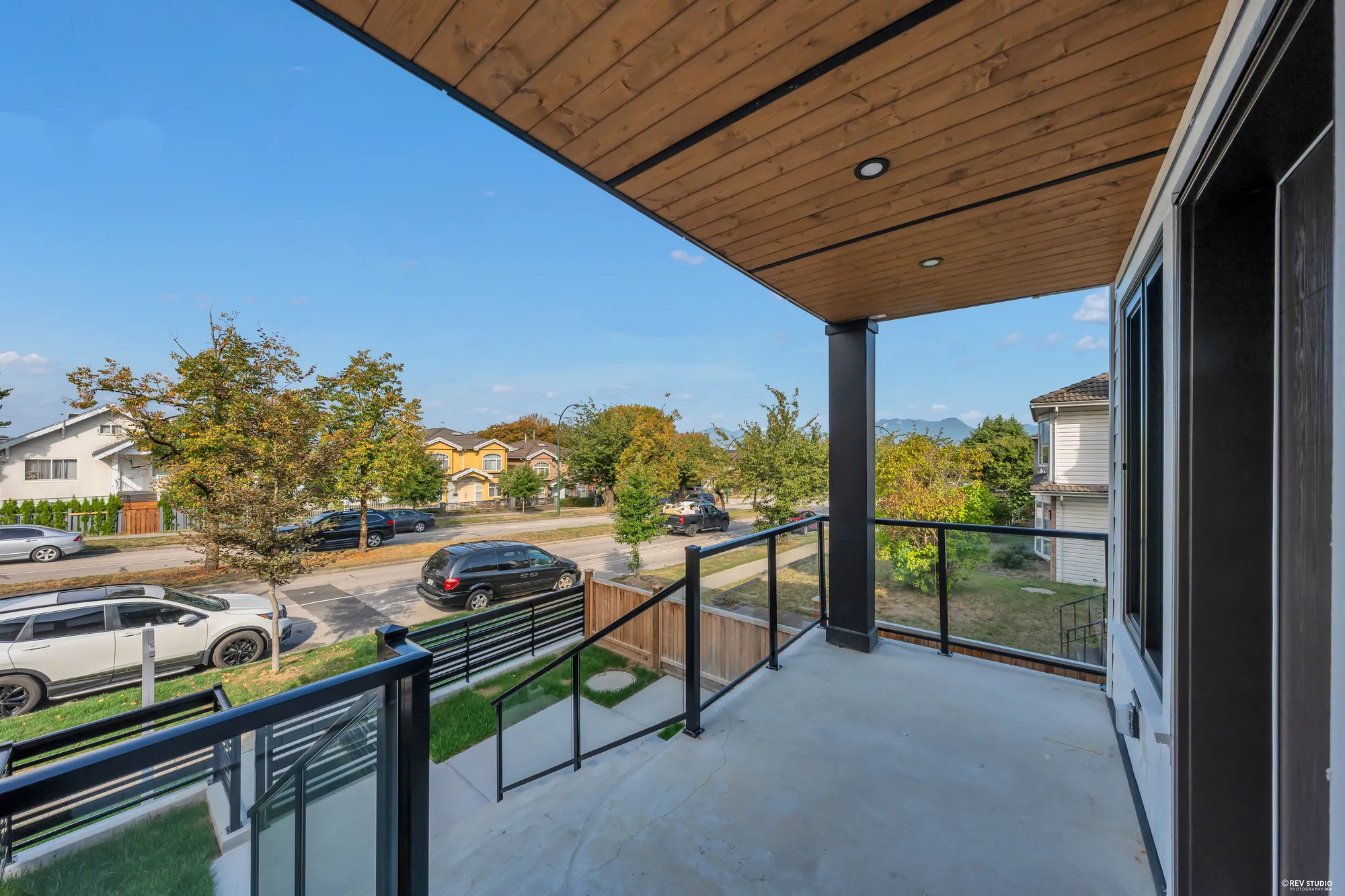 The covered front porch looking out to the street: a cedar ceiling, black railings, the houses opposite