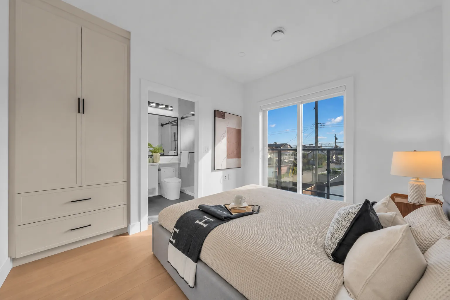 The primary bedroom toward its wardrobe wall and the open door to its bathroom, the window on the right