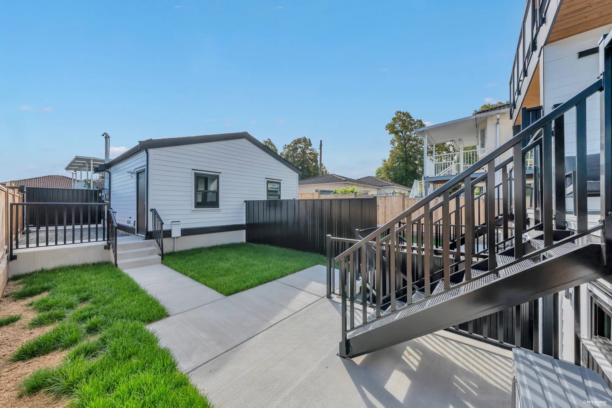 The yard from the foot of the porch stair: turf, a path to the garage, the cedar fence