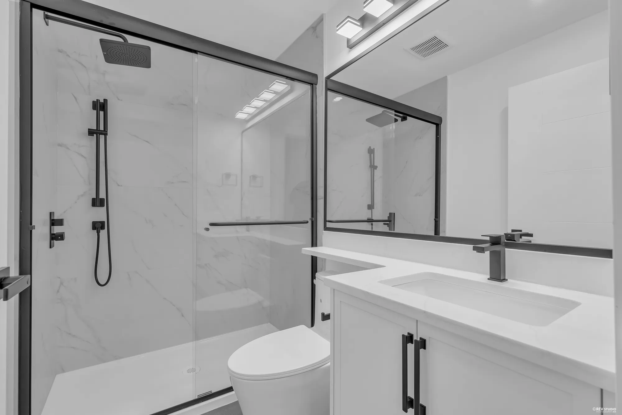The lower bathroom: a glass shower in marble-look tile, a white vanity, a mirror