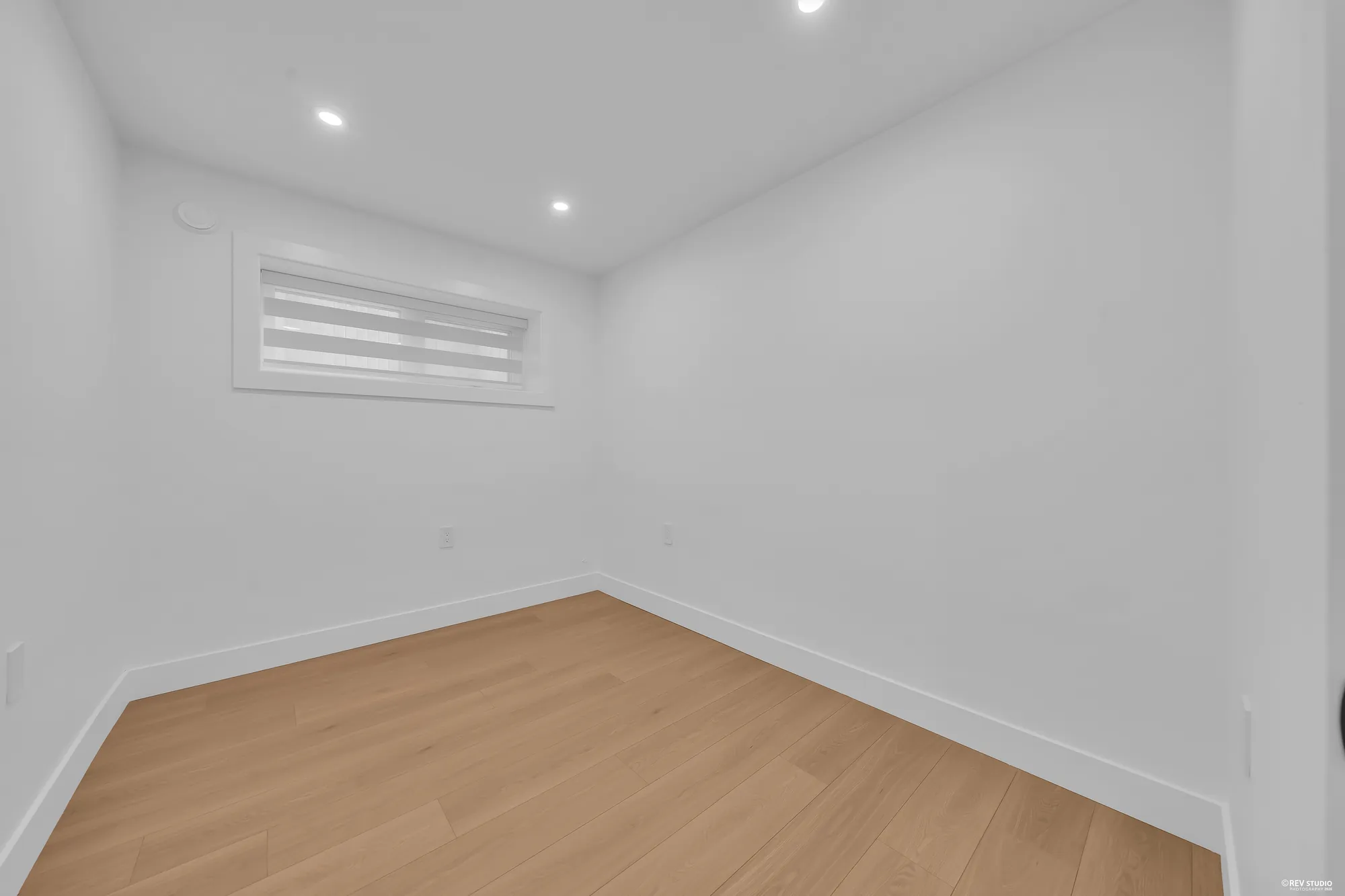 A lower bedroom: an empty room with laminate floor and a window with a blind