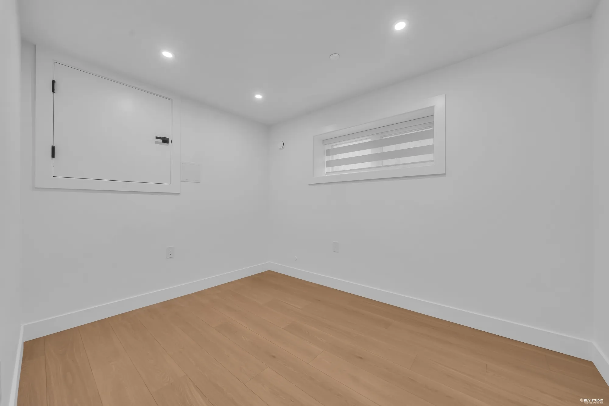 The second lower bedroom: an empty room with a window with a blind and an access panel in the wall