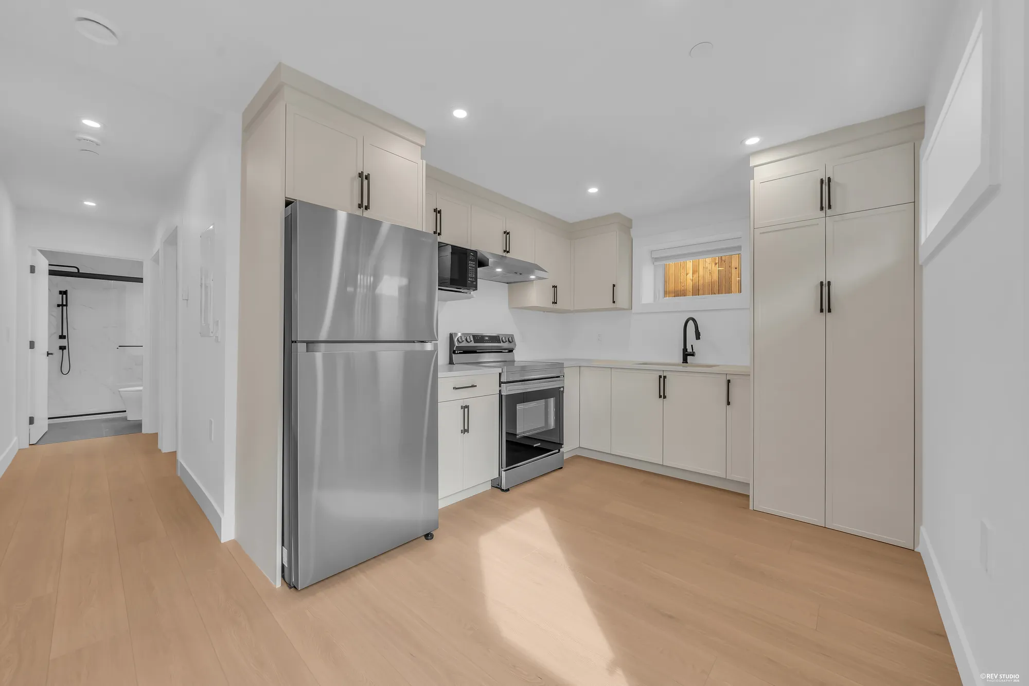 The lower eat-in kitchen: white cabinets, a stainless fridge and range, a window over the counter, the hall to the bedrooms