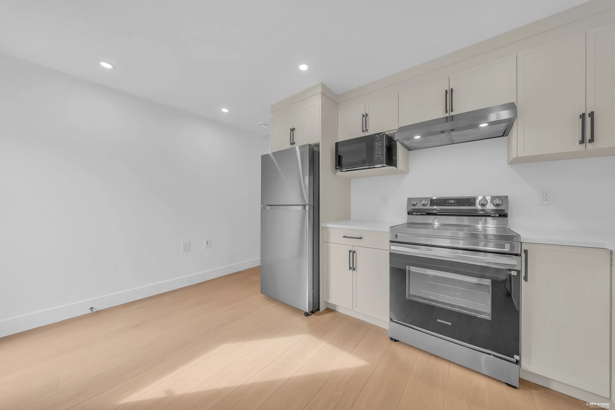 The lower kitchen from the door: the fridge, the range under its microwave, the window over the counter